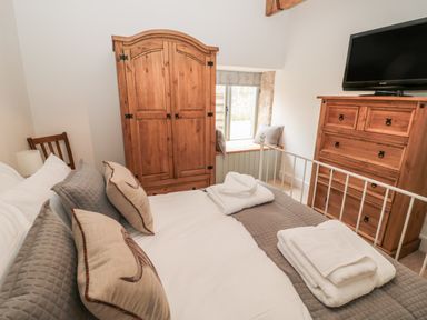A bedroom with a bed, wooden wardrobe, window seat, chest of drawers with a television at The Old Workshop in Middleton near Belford