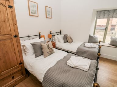 A bedroom with two single beds a wooden wardrobe and a window with cushions at The Old Workshop Middleton near Belford