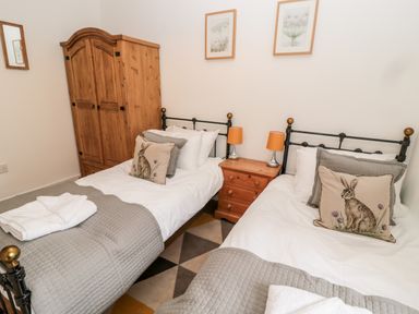 A bedroom with two single beds a wooden wardrobe and a bedside table with lamps at The Old Workshop in Middleton near Belford