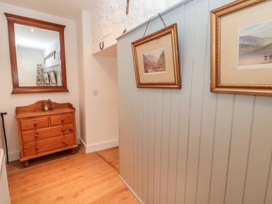 A hallway with a wooden chest of drawers a large wall mirror and framed paintings on a wooden paneled wall at The Old Workshop in Middleton near Belford