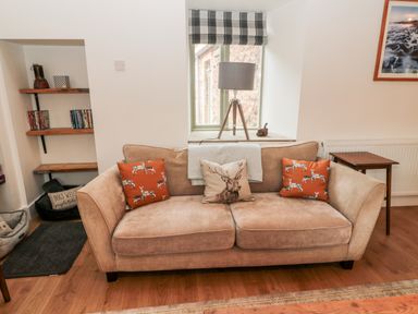 A living room with a beige sofa with animal print cushions a window lamp shelves and a small table at The Old Workshop in Middleton near Belford