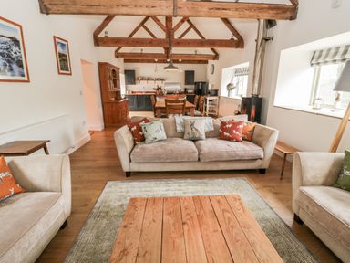 An open living room and kitchen with beige sofas wooden table wooden beams and large windows at The Old Workshop in Middleton near Belford