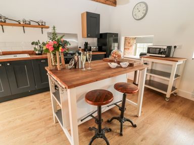 A kitchen with a wooden island and two stools a vase of flowers champagne glasses and a refrigerator at The Old Workshop in Middleton near Belford