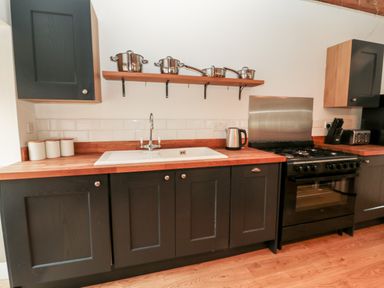 A kitchen with black cabinets wooden countertop a white sink stove and pots on a wooden shelf at The Old Workshop in Middleton near Belford