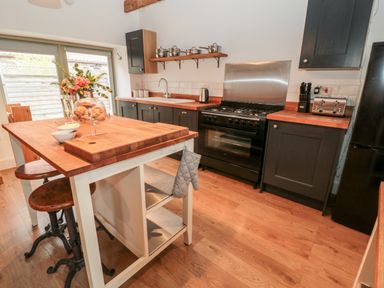 A kitchen with a wooden island table stools black cabinets and a black stove at The Old Workshop in Middleton near Belford