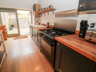 A kitchen with black cabinets wooden countertops a gas stove a knife block a toaster and a door leading outside at The Old Workshop in Middleton near Belford