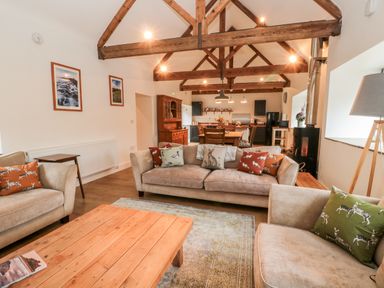 An open plan living room and kitchen with wooden beams on the ceiling and sofas with animal print cushions at The Old Workshop in Middleton near Belford