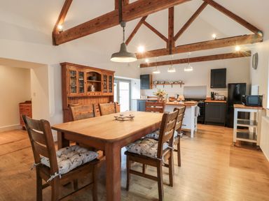 A kitchen and dining area with wooden table and chairs wooden beams and cupboards at The Old Workshop in Middleton near Belford
