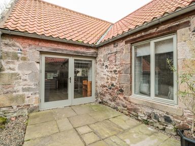 An outdoor stone patio with glass double doors and a window on a stone building with tiled roof at The Old Workshop in Middleton near Belford
