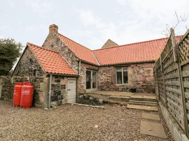An exterior view of a stone house with a tiled roof a wooden door stone steps and a gravel yard at The Old Workshop in Middleton near Belford