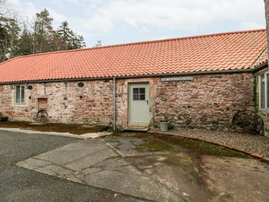 The exterior of a stone building with a red tiled roof a door a window and old wagon wheels at The Old Workshop in Middleton near Belford