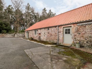 An exterior view of a stone building with a tiled roof and multiple doors with a paved area in front at The Old Workshop in Middleton near Belford
