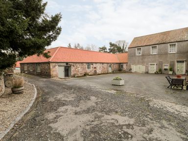 A courtyard with stone buildings and a gravel driveway at The Old Workshop in Middleton near Belford