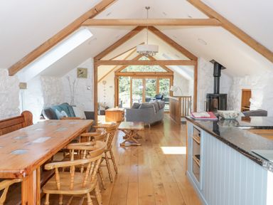 An open dining and living area with wooden table and chairs stone walls and large windows at Tyn Llwyn in Pencoed near Corwen