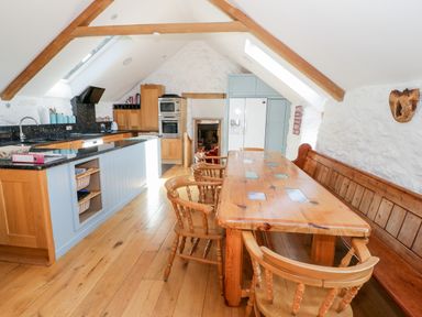 A kitchen and dining area with wooden floors wooden table wooden chairs and stone walls at Tyn Llwyn in Pencoed near Corwen