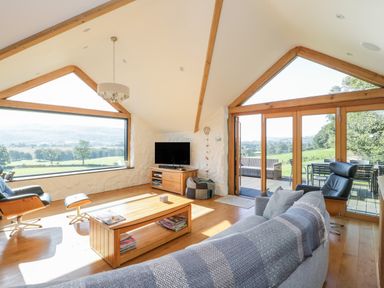 A living room with large windows and wooden furniture at Tyn Llwyn in Pencoed near Corwen