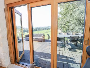 A wooden framed glass door leading to an outdoor patio with chairs a table and sofa at Tyn Llwyn in Pencoed near Corwen
