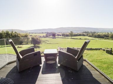 An outdoor deck with two wicker chairs and a small table overlooking a green field at Tyn Llwyn in Pencoed near Corwen