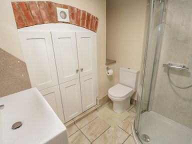 A bathroom with a toilet a corner shower a sink and white cabinets under a brick arch at Tyn Llwyn in Pencoed near Corwen