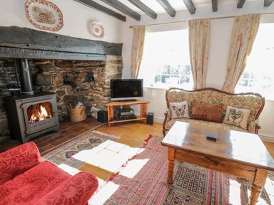 A living room with a stone fireplace wood stove television wooden table floral sofa and red armchair at Tyn Llwyn in Pencoed near Corwen