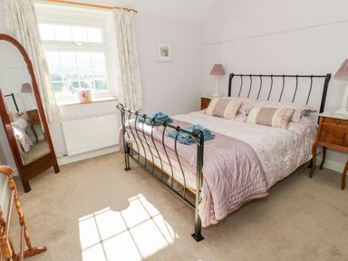 A bedroom with a metal bed frame two bedside tables with lamps a standing mirror window with curtains and a carpeted floor at Tyn Llwyn in Pencoed near Corwen