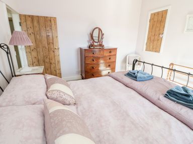 A bedroom with a bed with pink bedding a wooden dresser with a mirror a bedside table with a lamp and wooden doors at Tyn Llwyn in Pencoed near Corwen