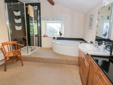 A bathroom with a corner bathtub shower enclosure wooden chair and sink with wooden cabinets at Tyn Llwyn Pencoed near Corwen