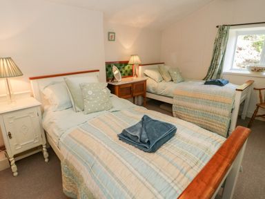 A bedroom with two single beds bedside tables lamps a window and a chair at Tyn Llwyn in Pencoed near Corwen