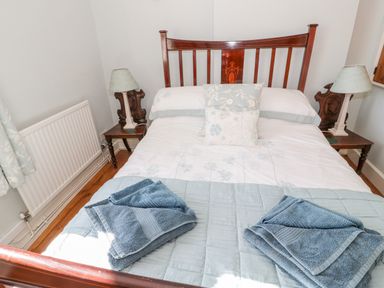 A bedroom with a wooden bed frame blue towels on bed and two lamps on bedside tables at Tyn Llwyn in Pencoed near Corwen