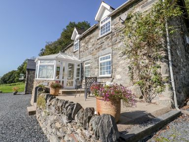 A stone house with a white conservatory and outdoor chairs on a patio with flower pots at Tyn Llwyn in Pencoed near Corwen