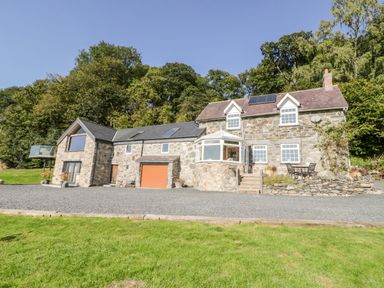 A stone house with a gravel driveway a patio area and green trees behind at Tyn Llwyn in Pencoed near Corwen