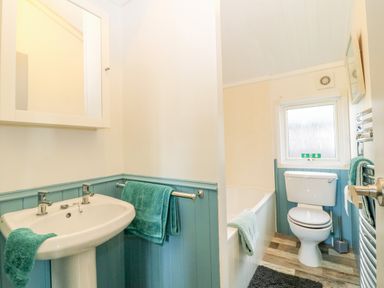 A bathroom with a sink a toilet a bathtub and teal towels at Smugglers Shack in Polperro