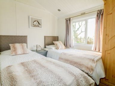 A bedroom with two single beds a bedside table a window with curtains and a wooden wardrobe at Smugglers Shack in Polperro