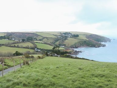 A coastal landscape with green fields houses and a dirt road leading to the sea at Smugglers Shack in Polperro