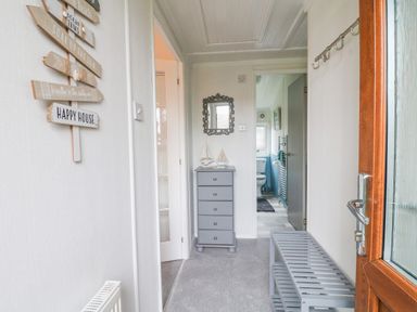 A hallway with a grey chest of drawers and mirror a door bench and hooks at Smugglers Shack in Polperro