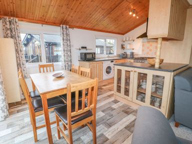 A kitchen and dining area with wooden table and chairs a washing machine microwave and glass cabinet at Smugglers Shack in Polperro