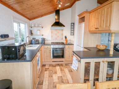 A kitchen with wooden cabinets black countertops a gas stove microwave toaster kettle and a wooden bowl at Smugglers Shack in Polperro