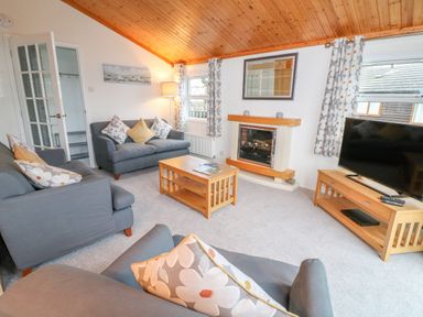 A living room with sofas, a coffee table, a fireplace, a television on a stand, and windows with curtains at Smugglers Shack in Polperro