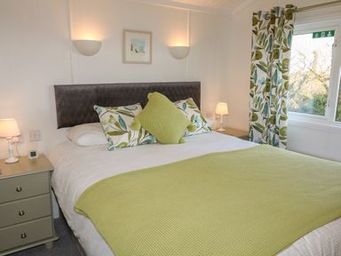 A bedroom with a bed with green and leaf patterned pillows and blanket next to nightstands with lamps at Smugglers Shack in Polperro