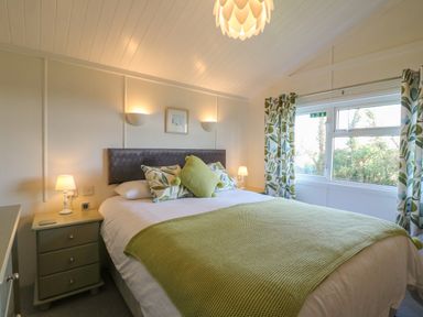 A bedroom with a bed green throw pillows and green patterned curtains at Smugglers Shack in Polperro