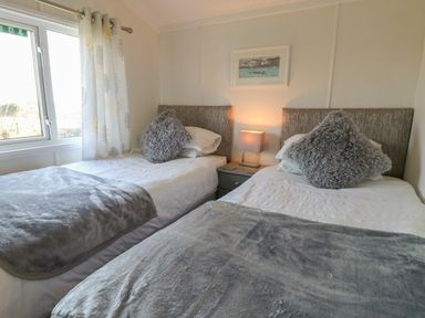 A bedroom with two single beds a bedside table with a lamp and a window with curtains at Smugglers Shack in Polperro