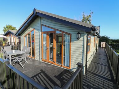 An outdoor deck with table and chairs attached to a single story cabin with large windows and wooden doors at Smugglers Shack in Polperro