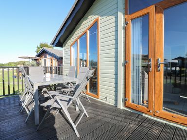 An outside deck with a metal table and six chairs attached to a building with large glass windows and wooden frames at Smugglers Shack in Polperro
