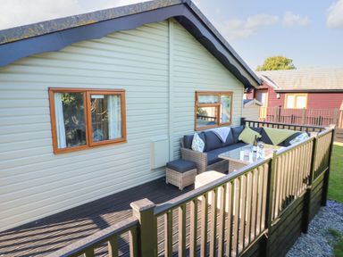 A deck with outdoor seating and a table next to a light green cabin with wooden windows at Smugglers Shack in Polperro