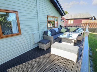 An outdoor seating area with a wicker sofa set and glass table on a wooden deck at Smugglers Shack in Polperro