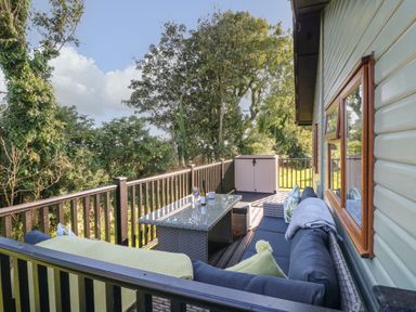 An outdoor deck with a wicker table and cushioned seating surrounded by trees at Smugglers Shack in Polperro