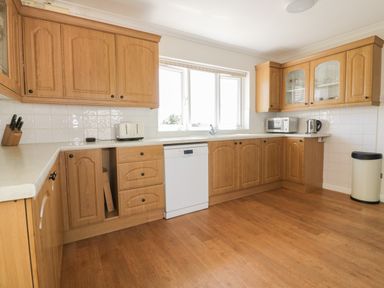 A kitchen with wooden cabinets a dishwasher a microwave kettle toaster and a knife block at Auverne Poundstock near Widemouth Bay