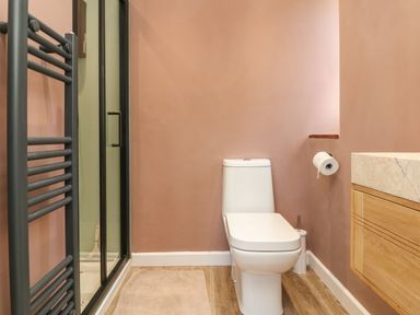 A bathroom with a white toilet a wooden vanity with a marble countertop a black towel rack and a glass shower door at Auverne in Poundstock near Widemouth Bay