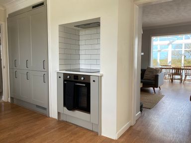 A kitchen area with built in oven and cupboards next to a dining room with wooden table and chairs at Auverne Poundstock near Widemouth Bay