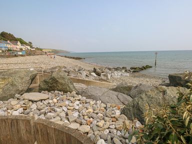 A pebble beach with large rocks and houses along the shore at Sarngwm in Narberth